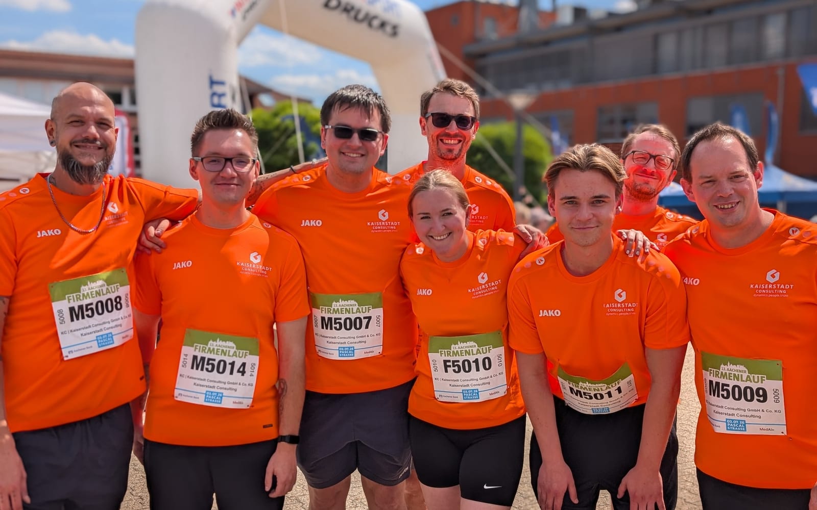 Das Team von KAISERSTADT Consulting beim 13. Aachener Firmenlauf, acht Personen in orangen Trikots mit Startnummern